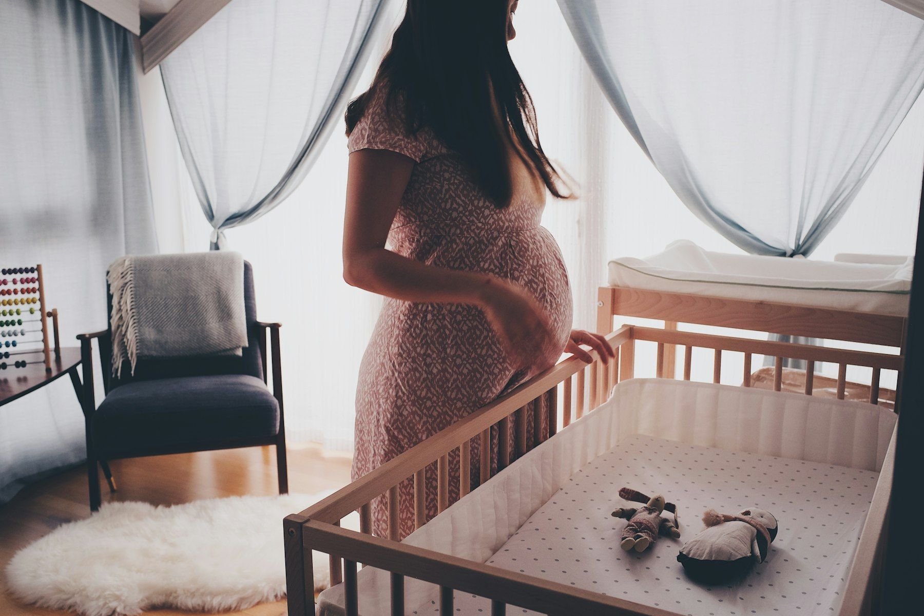Eine Schwangere steht im Kinderzimmer neben dem Babybett