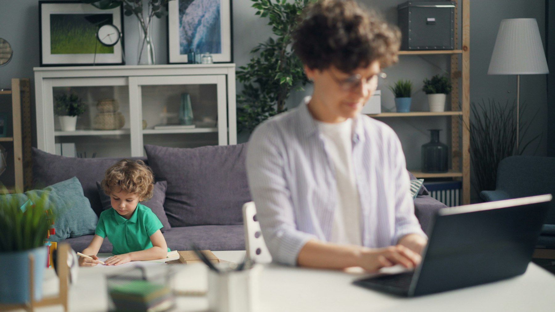 Eine Mutter arbeitet am Laptop, ihr Kind spielt im Hintergrund